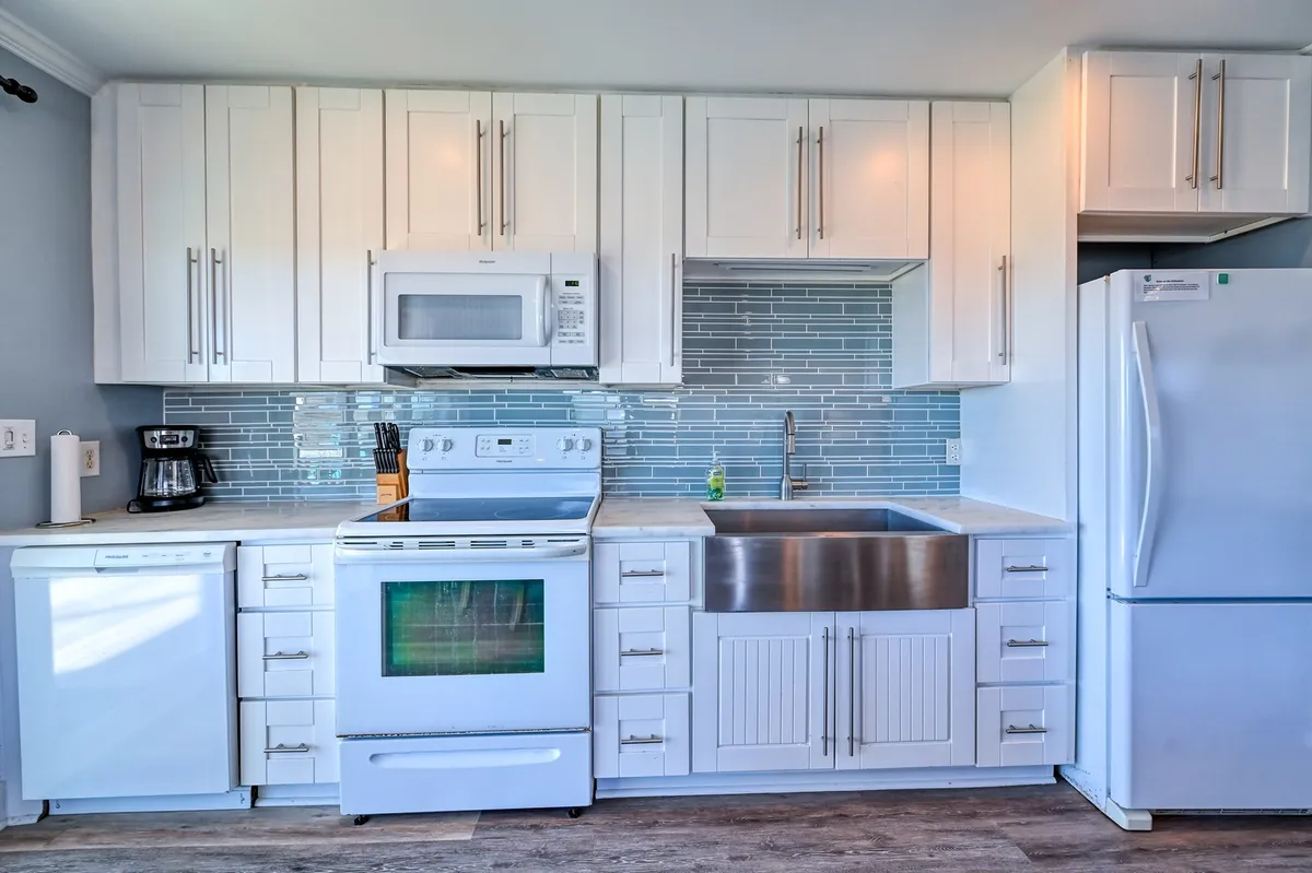 Another kitchen space featuring a stainless steel sink, white cabinetry, blue tile backsplash, and modern appliances. The setup feels both functional and stylish, supporting group or family cooking.