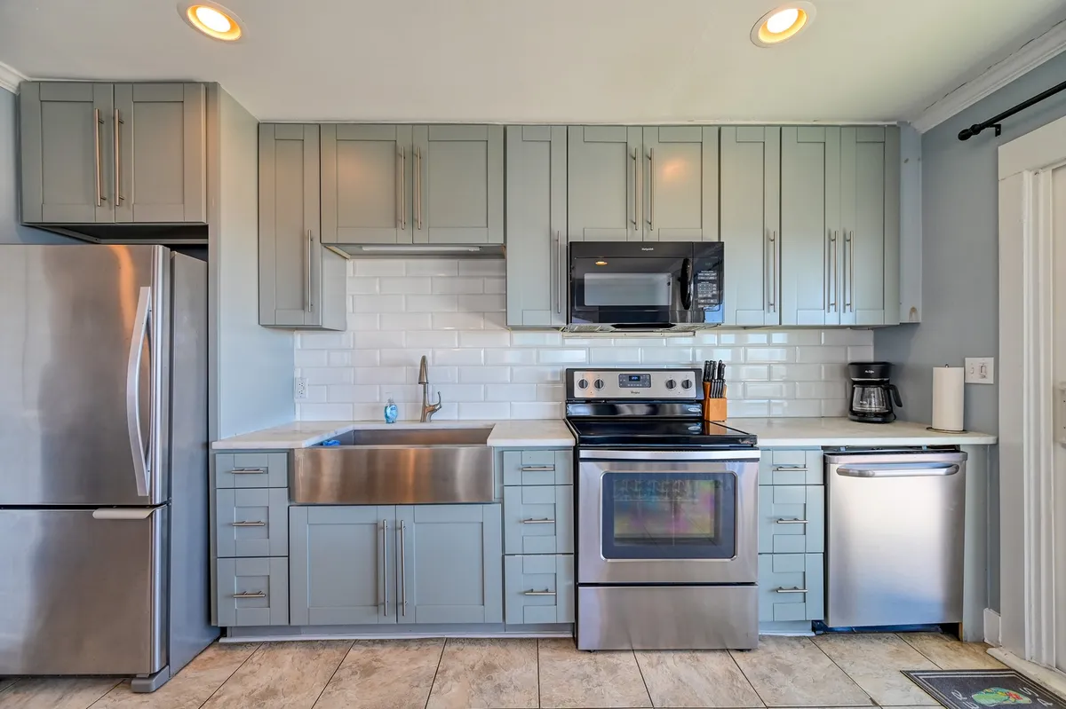 A kitchen scene with stainless steel appliances, a large farmhouse sink, and light blue cabinetry. The room feels welcoming and designed for both function and group gatherings.