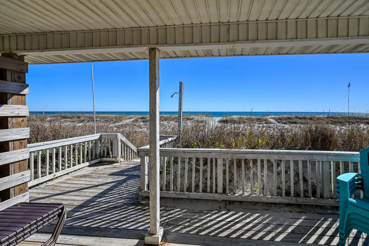 A serene oceanfront wooden deck bordered by beach grasses, offering sweeping views of the ocean. Outdoor lounge chairs and a table provide spots for relaxation or meals, with the tranquil sea stretching into the horizon.