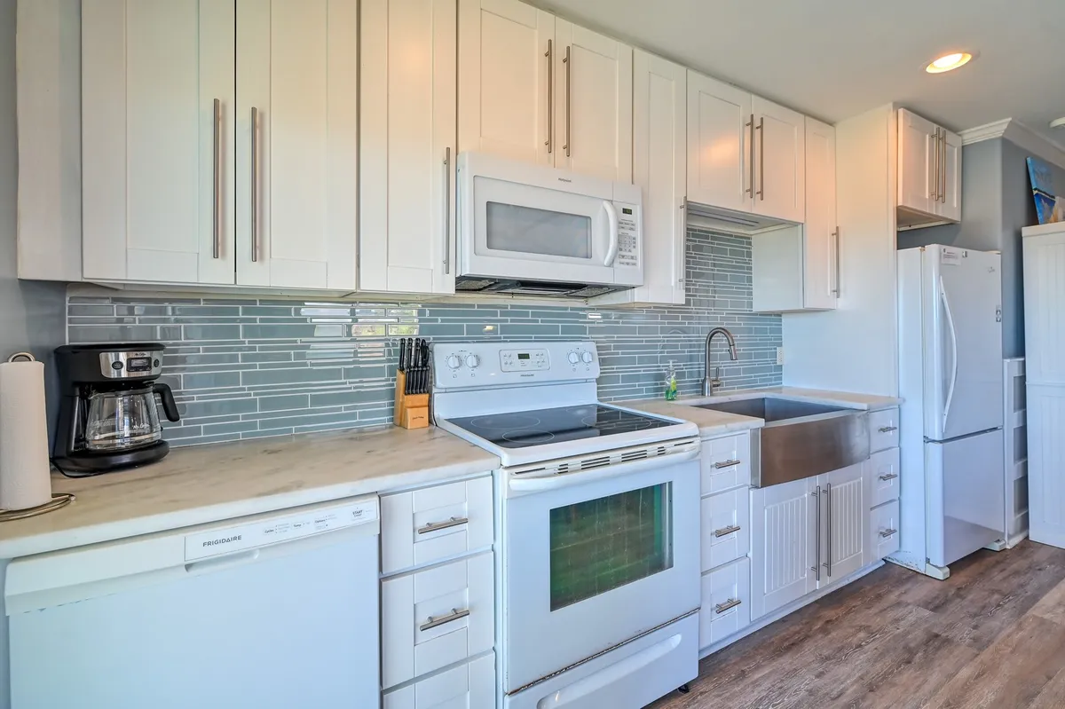This image showcases a modern kitchen with white cabinetry, stainless steel appliances, a marble countertop, and a classic subway tile backsplash. The space is bright, clean, and inviting, focusing on meal prep and culinary gatherings.