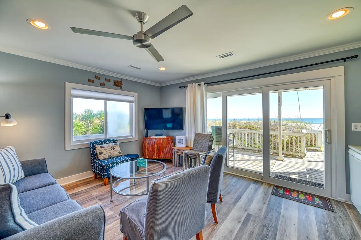 A spacious living area with a modern coffee table, comfortable sofas, and a large window offering an unobstructed ocean view. A television is positioned for group movie nights, and the seating is arranged to encourage conversation and relaxation. Natural light fills the room, creating a bright, inviting atmosphere.