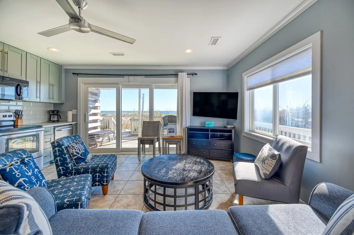 An open-plan living space with large windows offering expansive views, a comfortable seating area perfect for unwinding after a day out, and a glimpse of modern kitchen appliances. Decorative pillows and natural light evoke a connection to the outdoors.