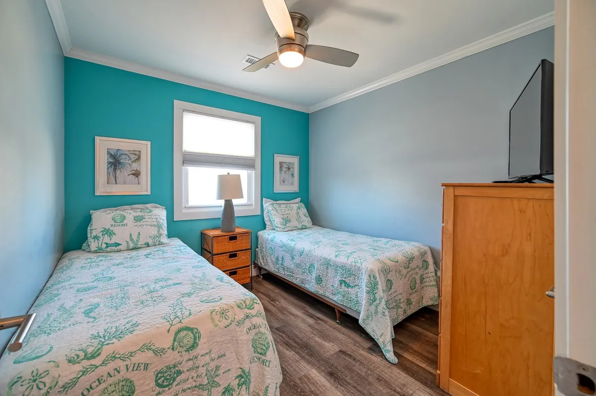 A cheerful twin bedroom with two twin beds, a lampshade, decorative wall art, and a television. The space is cozy, inviting, and ideal for kids or guests seeking a playful yet restful retreat.