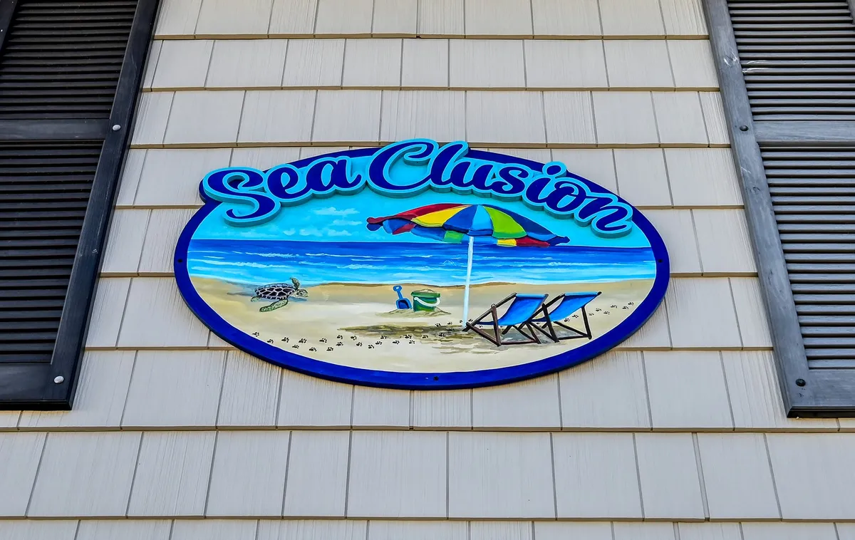 This cheerful exterior image captures a colorful sign with a beach scene illustration, a sunny umbrella, and lounge chairs arranged for family or group enjoyment. The atmosphere is bright, playful, and inviting, evoking memories of shared beach days and group activities.